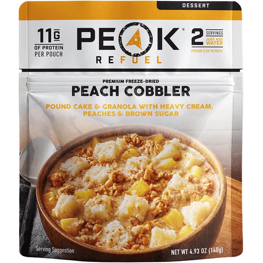 A single serving pouch of Peak Refuel Peach Cobbler dessert, featuring a white and orange package design with a bowl of the prepared peach cobbler shown on the front.