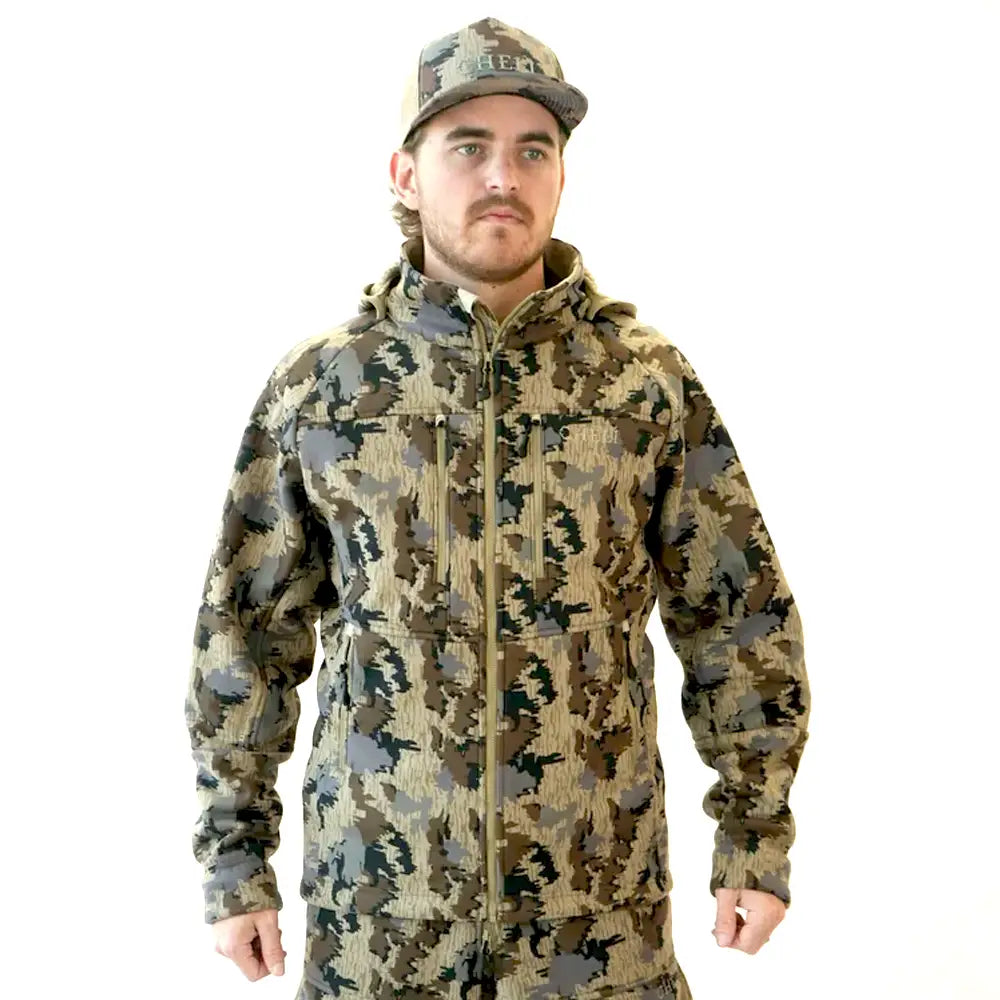 A man wearing a camouflage hooded jacket and matching camouflage cap, standing against a plain white background.