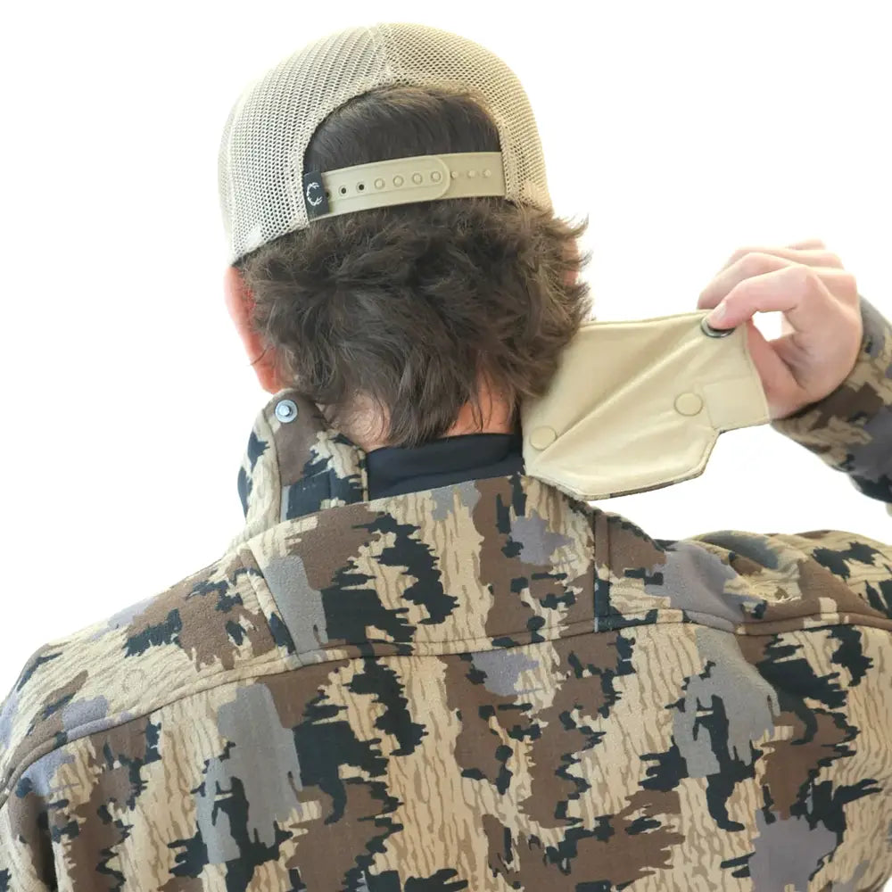A man shown from behind wearing a camouflage jacket and a beige trucker hat.