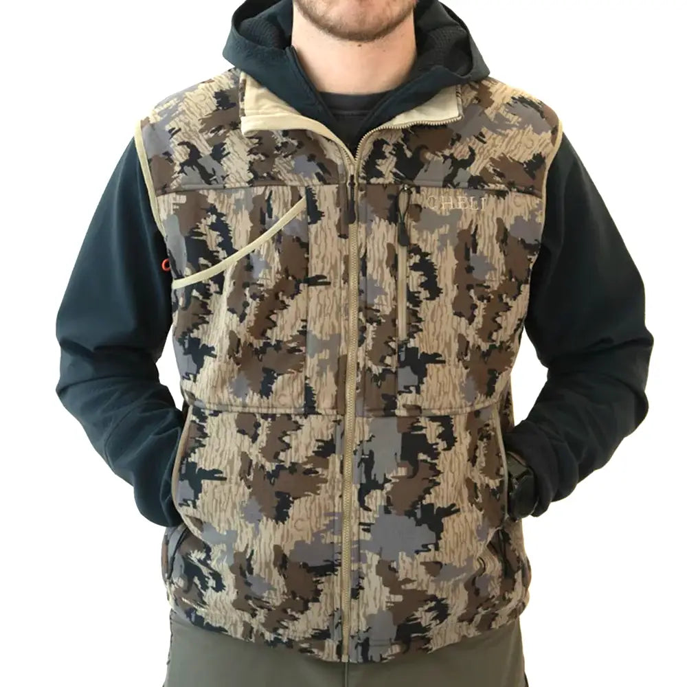 A man wearing a camouflage-patterned zip-up vest over a dark hoodie, shown from the neck down against a plain white background.