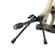 Compact black carbon fiber tripod bow stand attached to tan recurve bow riser.